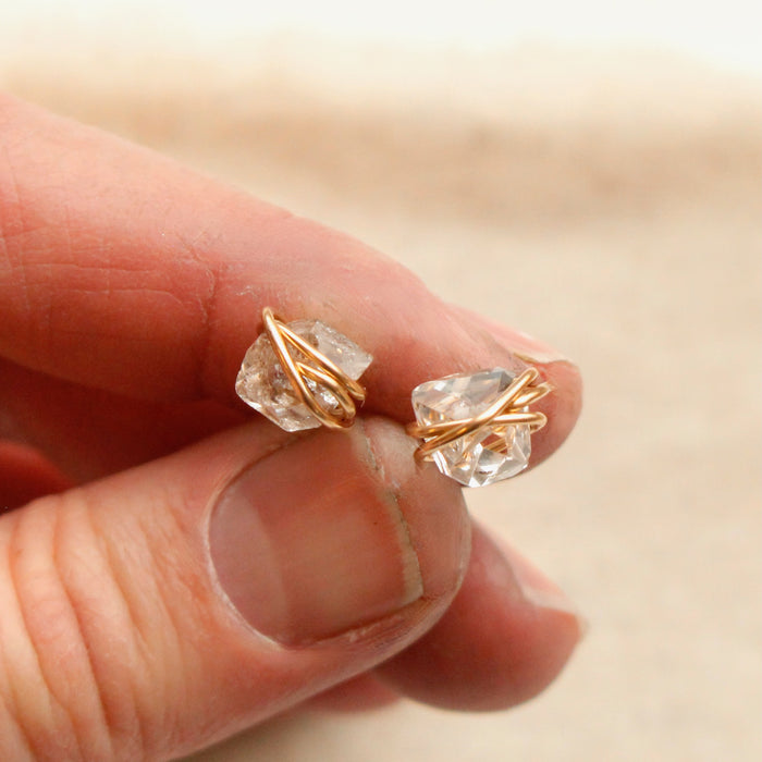 The gold wrapped herkimer diamond post earrings being held