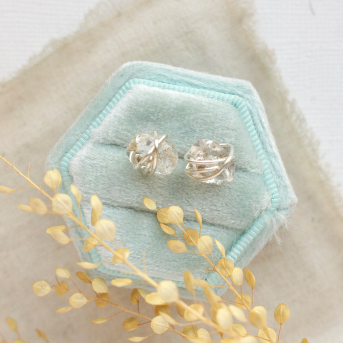The silver wrapped herkimer diamond post earrings styled on a velvet box with linen and dried grass