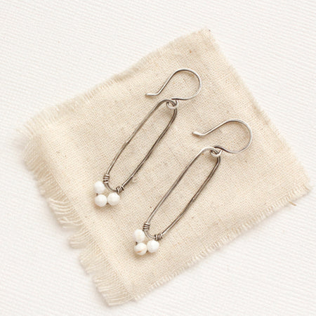 The white howlite wrapped forged silver long hoop earrings style on tan linen