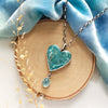 The hubei turquoise heart and grandidierite necklace styled on wood with blue velvet and dried grass