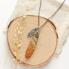 The red creek jasper and feather necklace styled on wood with dried grass and tan linen