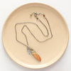 The jasper and silver feather necklace styled on a tan plate to show the adjustable lobster clasp closure