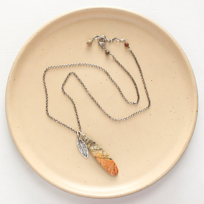 The jasper and silver feather necklace styled on a tan plate to show the adjustable lobster clasp closure