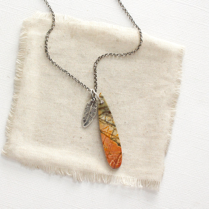 The red creek jasper and silver feather charm necklace styled on tan linen