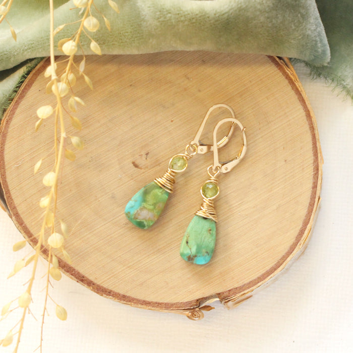 The kingman turquoise & peridot earrings styled on wood with green velvet and dried grass