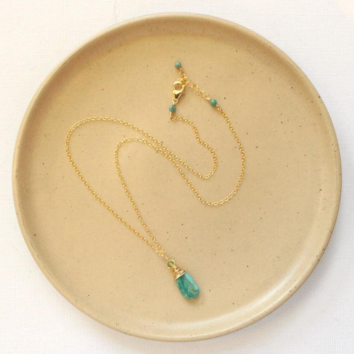The kingman turquoise and peridot necklace styled on a tan plate to show the adjustable lobster clasp closure