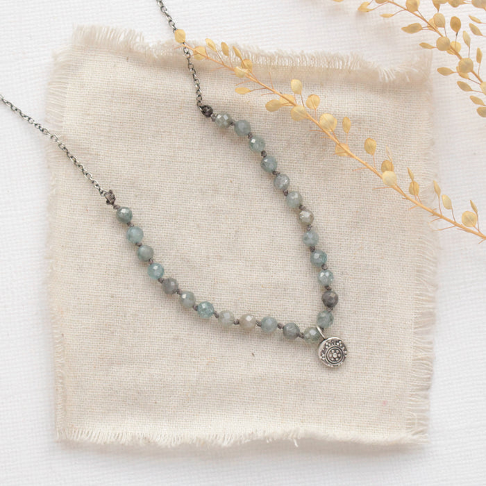 The knotted zircon roma necklace styled on tan linen with dried grass