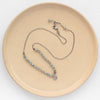 The knotted zircon roma necklace styled on a tan plate to show the adjustable lobster clasp closure