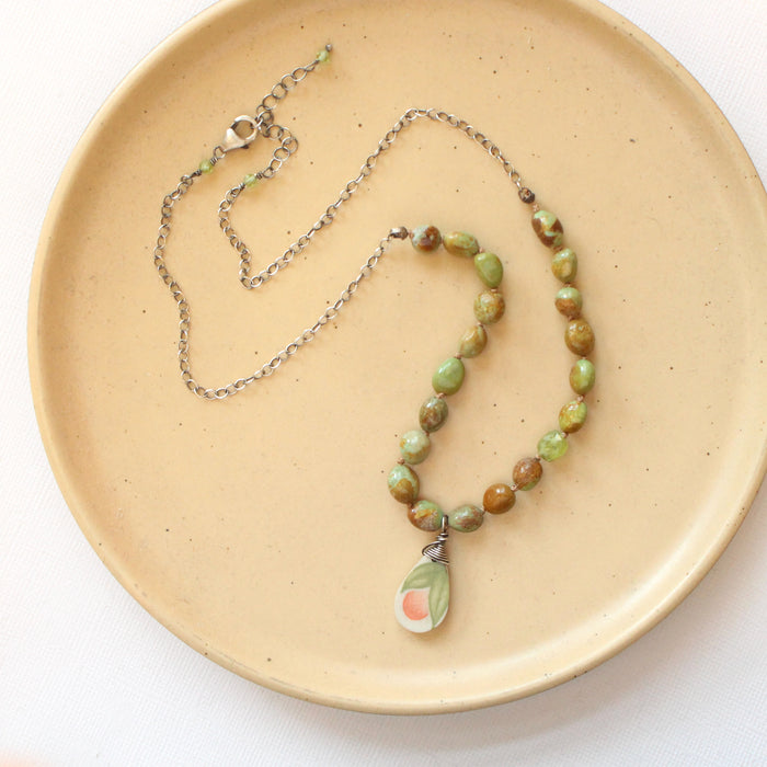 The knotted elisa turquoise, peridot, and peach blossom necklace styled on a tan plate to show the adjustable lobster clasp closure