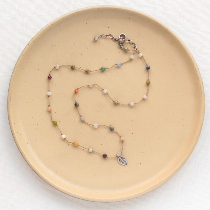 The knotted kaleidoscope leaf necklace styled on a tan plate to show the adjustable lobster clasp closure