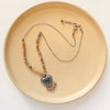 The knotted moonstone heart necklace styled on a tan plate to show the adjustable lobster clasp closure