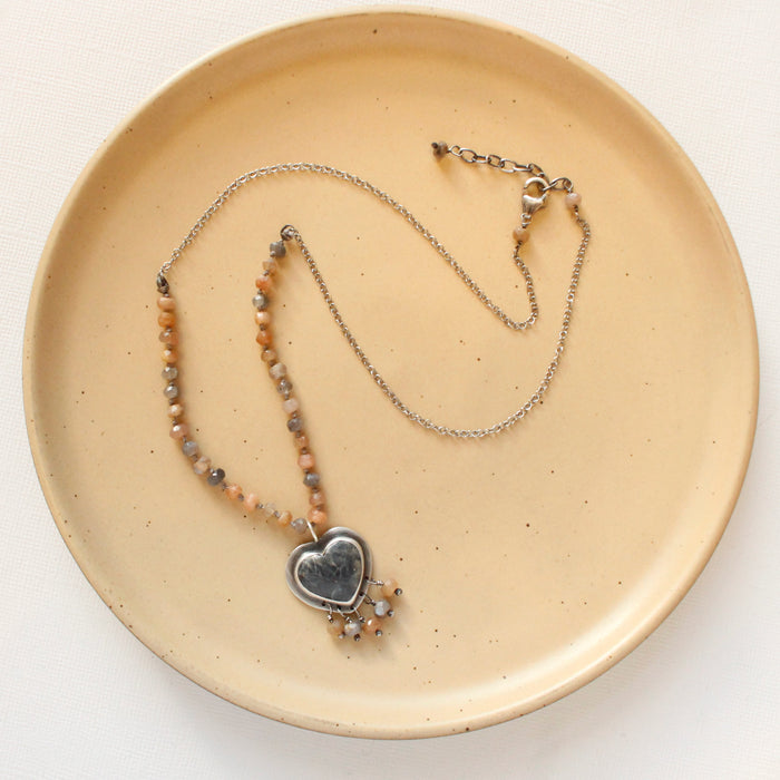 The knotted moonstone heart necklace styled on a tan plate to show the adjustable lobster clasp closure