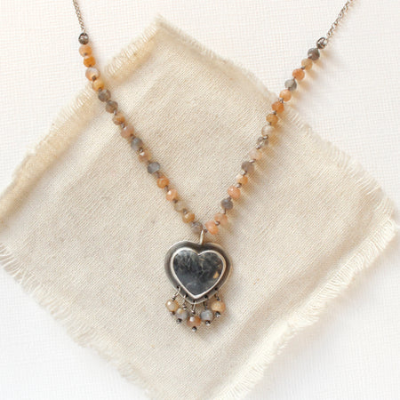The knotted moonstone heart necklace styled on tan linen