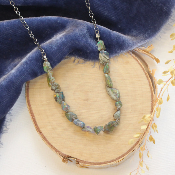 The knotted opal necklace styled on wood with blue velvet and dried grass