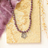 The knotted purple ruby layered cactus flower necklace styled on a tan rock with purple velvet and dried grass