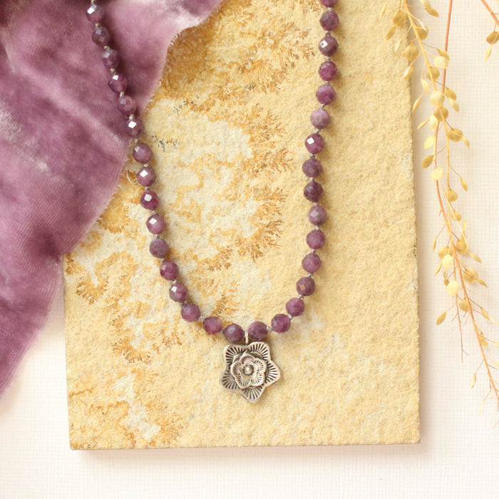 The knotted purple ruby layered cactus flower necklace styled on a tan rock with purple velvet and dried grass
