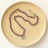 The knotted purple ruby layered cactus flower necklace styled on a tan plate to show the adjustable lobster clasp closure