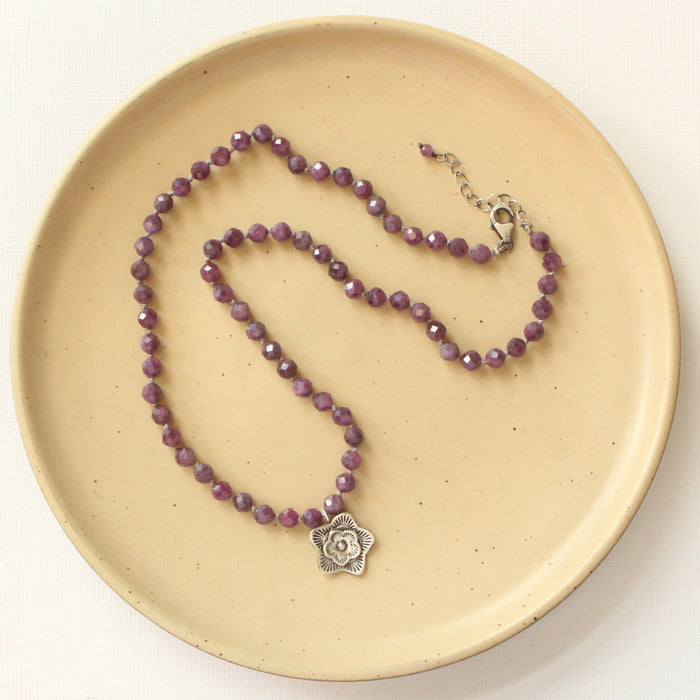 The knotted purple ruby layered cactus flower necklace styled on a tan plate to show the adjustable lobster clasp closure