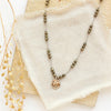 The knotted pyrite and mini bronze flower necklace styled on a tan rock with linen and dried grass