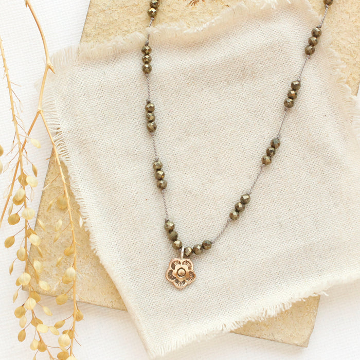 The knotted pyrite and mini bronze flower necklace styled on a tan rock with linen and dried grass