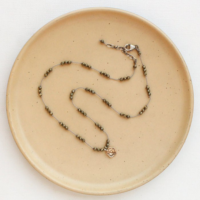 The knotted pyrite and bronze mini cactus flower necklace styled on a tan plate to show the adjustable lobster clasp closure