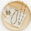 The knotted pyrite and mini bronze cactus flower necklace styled on a tan plate with the matching bracelet and earrings