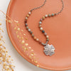 The knotted rainbow agate sun cross necklace styled on an orange plate with dried grass