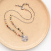 The knotted rainbow agate sun cross necklace styled on a tan plate to show the adjustable lobster clasp closure