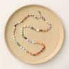 The knotted rainbow opal necklace styled on a tan plate to show the adjustable lobster clasp closure