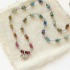 The knotted rainbow tourmaline heart necklace styled on tan linen