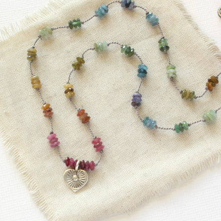 The knotted rainbow tourmaline heart necklace styled on tan linen