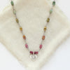 The knotted rainbow tourmaline heart necklace styled on tan linen