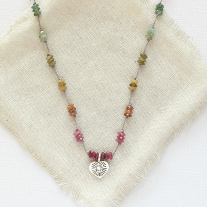 The knotted rainbow tourmaline heart necklace styled on tan linen