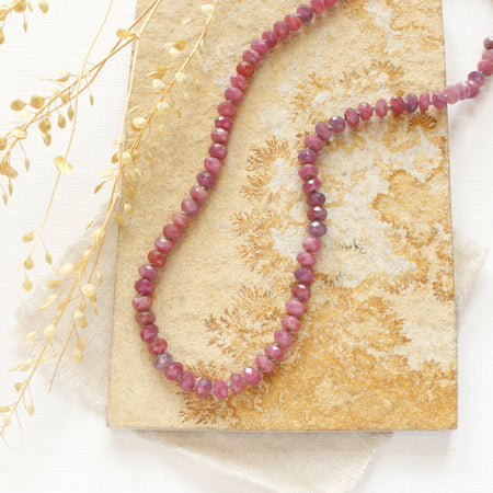 The knotted ruby necklace styled on a tan rock with tan linen and dried grass