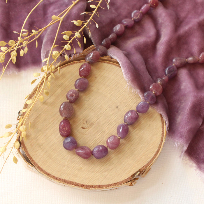 The knotted ruby necklace styled on wood with purple velvet and dried grass