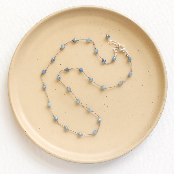 The knotted aquamarine necklace styled on a tan plate to show the adjustable lobster clasp closure