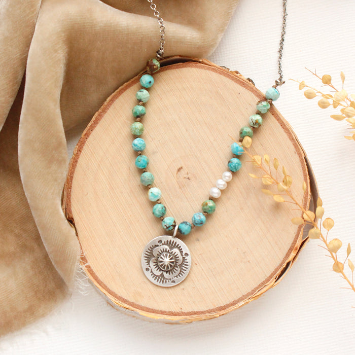 The knotted seaside columbine medallion necklace styled on wood with tan velvet and dried grass