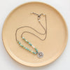 The knotted seaside columbine medallion necklace styled on a tan plate to show the adjustable lobster clasp closure