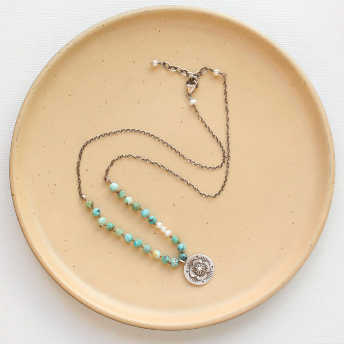 The knotted seaside columbine medallion necklace styled on a tan plate to show the adjustable lobster clasp closure