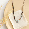 The knotted serenity soar necklace styled on a tan plate with linen and dried grass