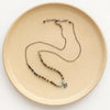 The knotted serenity soar necklace styled on a tan plate to show the adjustable lobster clasp closure
