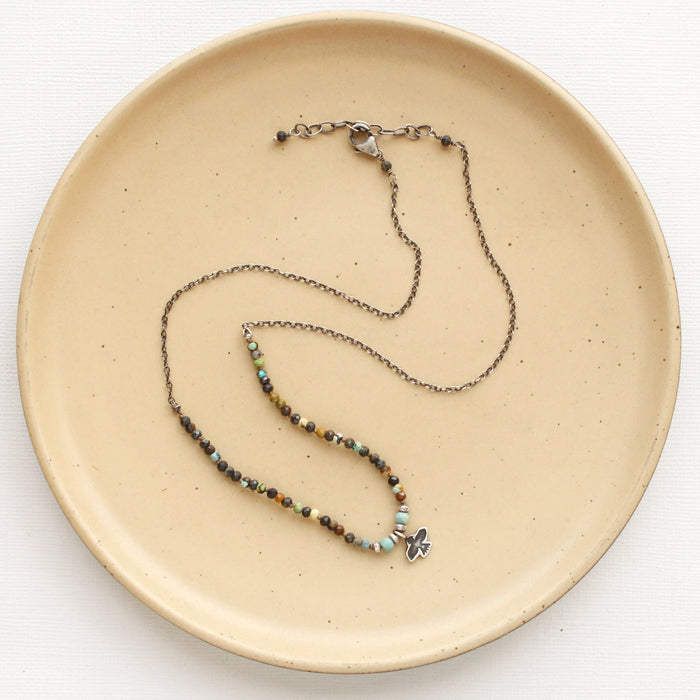 The knotted serenity soar necklace styled on a tan plate to show the adjustable lobster clasp closure