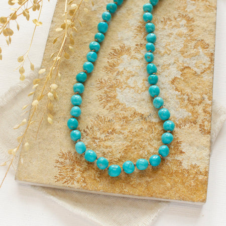 The knotted sleeping beauty turquoise necklace styled on a tan rock with linen and dried grass