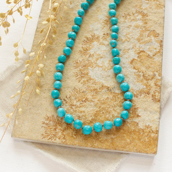 The knotted sleeping beauty turquoise necklace styled on a tan rock with linen and dried grass