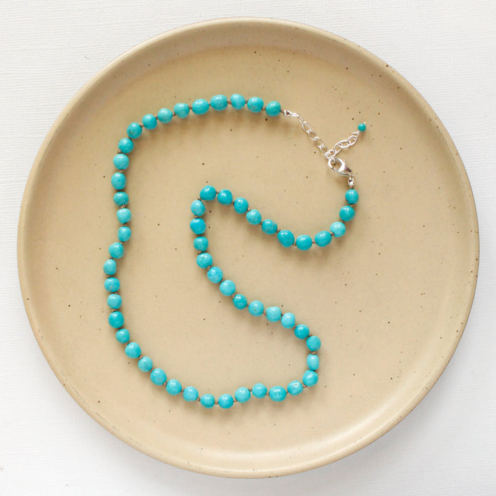 The knotted sleeping beauty turquoise necklace styled on a tan plate to show the silver adjustable lobster clasp closure 