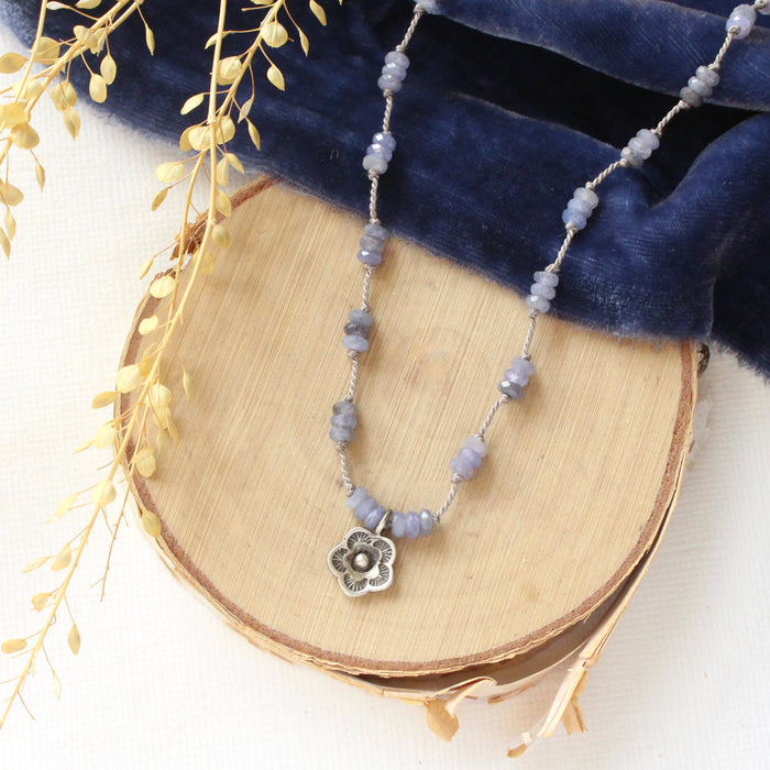 The knotted tanzanite mini cactus flower necklace styled on wood with blue velvet and dried grass