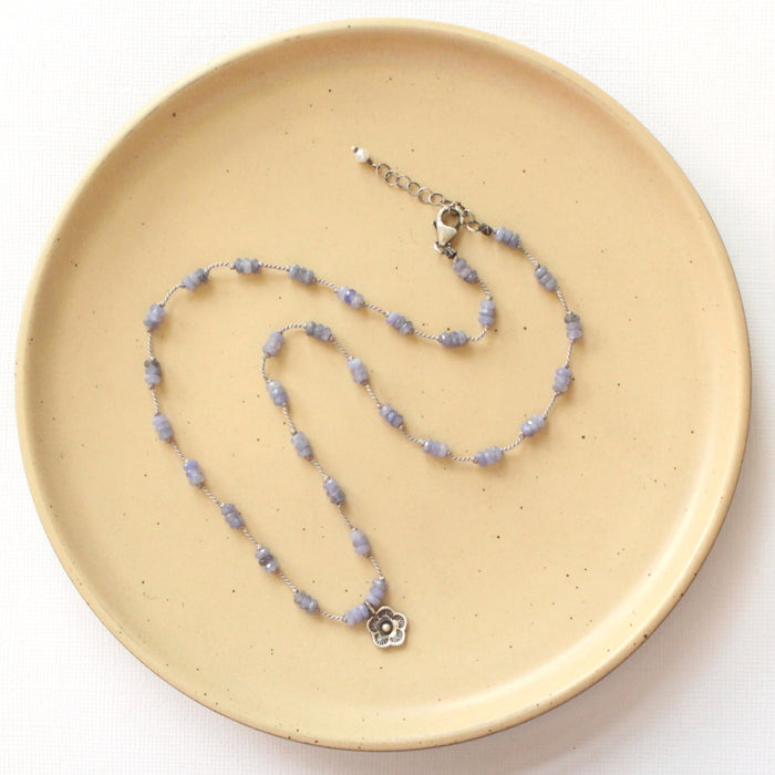 The knotted tanzanite mini cactus flower necklace styled on a tan plate to show the adjustable lobster clasp closure