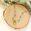 The knotted turquoise and peridot drop necklace styled on wood with green velvet and dried grass