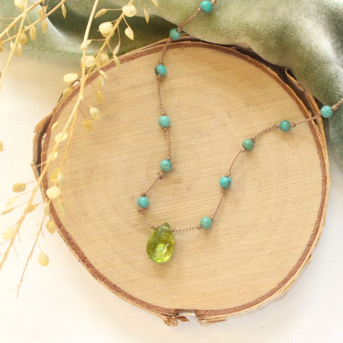 The knotted turquoise and peridot drop necklace styled on wood with green velvet and dried grass