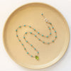 The knotted turquoise and peridot drop necklace styled on a tan plate to show the adjustable lobster clasp closure